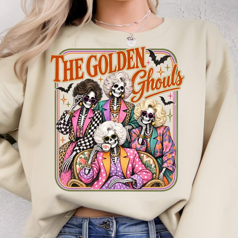 A woman wearing a white sweater with a graphic design featuring four stylized female characters with skeletal features, dressed in colorful outfits and accessories, with the text "The Golden Ghouls" above them.