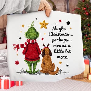 Peut inclure: Coussin blanc avec broderie du Grinch et d'un chien sur le thème de Noël. Le Grinch porte un pull et une écharpe rouges, et le chien a des bois de renne. Le texte dit : "Maybe Christmas... perhaps... means a little bit more."