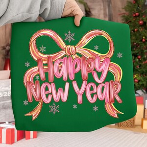 May include: A green pillow with a pink and gold bow design and the words "Happy New Year" in pink script. The pillow also features small snowflake accents, perfect for holiday decor.