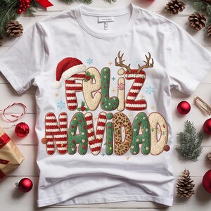 K&ouml;nnte beinhalten: Wei&szlig;es T-Shirt mit dem Schriftzug "Feliz Navidad" in einem festlichen Design. Der Text zeigt einen Weihnachtsmannhut, Rentiergeweihe und einen Buchstaben mit Leopardenmuster. Weihnachts-Themenbekleidung.