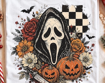 May include: A white t-shirt featuring a graphic print of a ghost-like mask in a dark hood, surrounded by red and orange roses, white flowers, two jack-o'-lanterns, a knife, bats, and a black and white checkered pattern in the background.