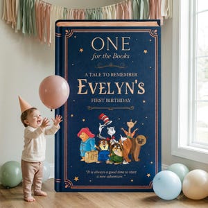 May include: A large, rectangular, dark blue book-shaped sign with gold lettering that reads: ONE for the Books, A TALE TO REMEMBER EVELYN'S FIRST BIRTHDAY, and It is always a good time to start a new adventure. It features illustrations of storybook characters.