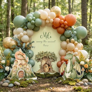 May include: A whimsical party scene with a balloon arch in shades of green, gold, and orange. A sign reads "Milo among the ancient trees." Decorative cutouts include a dragon, a castle, and a tree with a door.