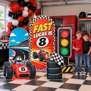 May include: A race car themed party display featuring a large arch sign with the text FAST LUCAS IS 8, a red race car cutout with the number 8, a traffic light stand, and a stack of tires with a checkered flag.