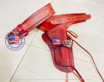 May include: A red leather gun holster and belt set. The holster features a decorative pattern and a silver buckle. The belt is also red and has a matching design. The set is likely for a toy gun or costume.