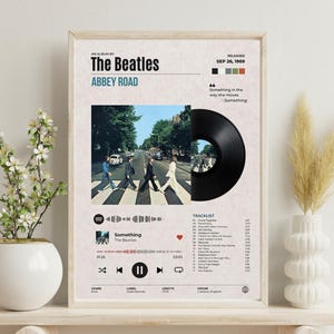 May include: A rectangular poster featuring The Beatles Abbey Road album art, a black vinyl record graphic, a tracklist, and a digital music player interface. The design includes the album title, release date, and song lyrics on a light background.