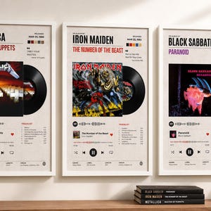 May include: Three framed wall posters featuring music album art for Metallica, Iron Maiden, and Black Sabbath. Each print displays a vinyl record graphic, tracklist, release date, and song information in a clean, minimalist layout on a beige background.