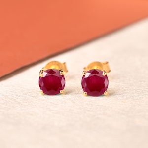 Pode incluir: Um par de brincos de tarracha com rubis redondos facetados de cor vermelho profundo cravados em ouro amarelo. Cada rubi é preso por quatro pequenas garras, exibindo um corte brilhante que reflete a luz. São um par de brincos a combinar.