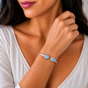 May include: A silver cuff bracelet featuring two teardrop-shaped light blue stones at each open end. The metal band has a smooth, polished finish, and the stones display a marbled texture with varying shades of sky blue and white throughout.