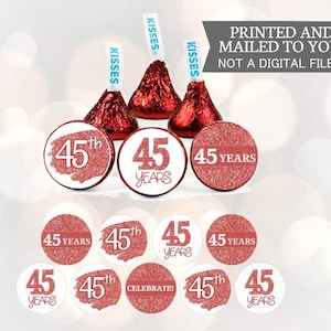 May include: A set of 10 round, white, adhesive labels with a rose gold glitter background. The labels feature the text "45th" or "45 Years" in white. The labels are designed for use on Hershey's Kisses chocolates.