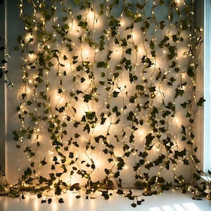 May include: A decorative string of warm white LED lights entwined with artificial ivy vines. The green leaves and small lights create a soft, ambient glow, ideal for home decor or event styling. The lights are evenly spaced along the vines.
