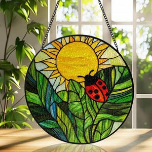 Puede incluir: Atrapasoles redondo de vidriera con un sol amarillo, follaje verde y una mariquita roja con lunares negros. El atrapasoles está enmarcado en negro y cuelga de una cadena. Artículo decorativo para ventana o pared.