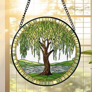 May include: Round stained glass window art featuring a weeping willow tree scene. The artwork has a black metal frame and a chain for hanging. The tree has a brown trunk and green leaves, with a lake and hills in the background.