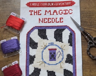 Peut inclure: Un projet de point de croix intitulé "The Magic Needle" avec un motif de vache, une bordure violette et bleue, et le texte "Choose Your Own Adventure". Le projet est accompagné de bobines de fil DMC rouges, violettes et marron et de ciseaux décoratifs.