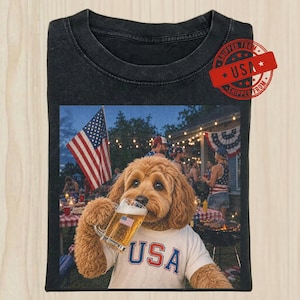 May include: A black t-shirt featuring a graphic of a golden-colored dog wearing a white t-shirt with the text USA in blue and red letters. The dog is holding a glass mug of beer with a small American flag decal. The background shows a backyard party.