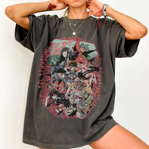 May include: Dark gray t-shirt featuring a colorful anime-style graphic. The graphic includes multiple characters in various poses, surrounded by a pink floral design. The shirt has a vintage, worn look.