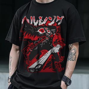 May include: Black t-shirt featuring a red and white graphic design. The design includes Japanese text, a character in a red suit, and a monster with multiple eyes. The shirt has short sleeves and a crew neck.