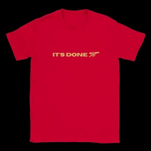 Puede incluir: Camiseta roja con el texto dorado "IT'S DONE" y un cañón dorado. La camiseta tiene cuello redondo y mangas cortas. El diseño está centrado en la parte delantera.