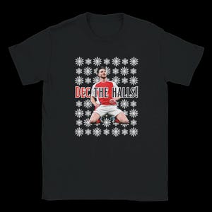 Puede incluir: Camiseta negra con un futbolista con camiseta roja y blanca, arrodillado con los brazos levantados. El texto "DEC THE HALLS!" es rojo y blanco, rodeado de copos de nieve blancos. Un diseño festivo navideño.
