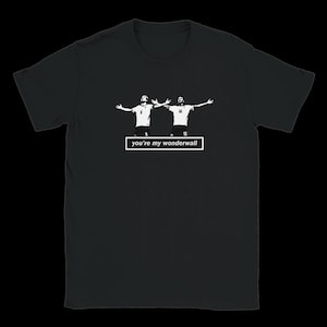 Könnte beinhalten: Ein schwarzes T-Shirt mit kurzen Ärmeln und einer weißen Grafik von zwei Fußballspielern, die ihre Arme jubelnd ausstrecken. Unter den Figuren befindet sich ein weißer rechteckiger Kasten mit dem schwarzen Text "you're my wonderwall".