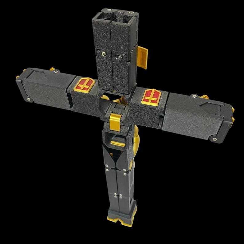 May include: A black and gold cross with a detailed design. The cross features gold accents and red emblems. The cross is made of multiple pieces and has a complex, mechanical appearance. The background is black.