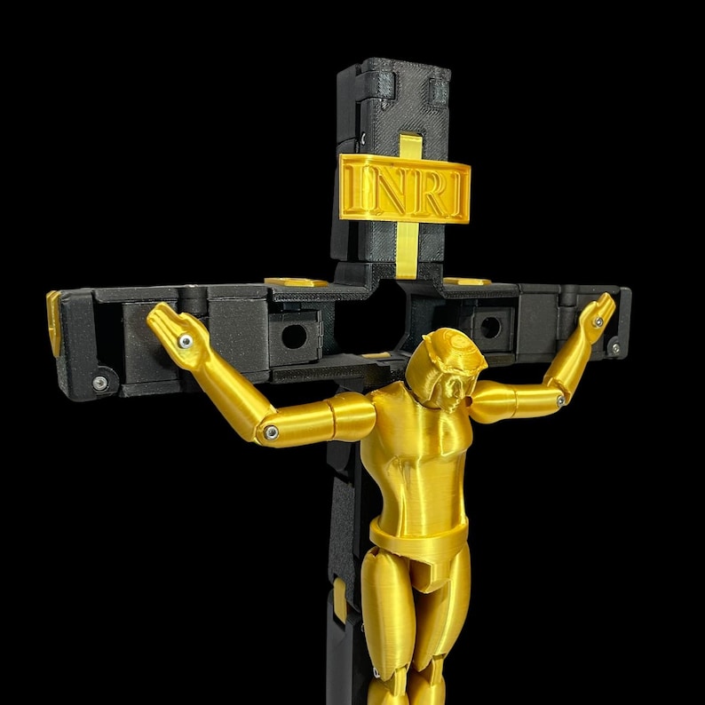 May include: A gold-coloured articulated figure on a black cross with a gold INRI sign. The figure has its arms outstretched. The cross is black with gold accents. The background is black.