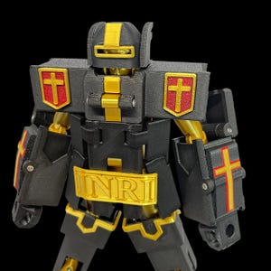 May include: A black and gold robot toy with red cross emblems. The robot has the letters INRI on its chest. The toy is made of plastic and has articulated joints.