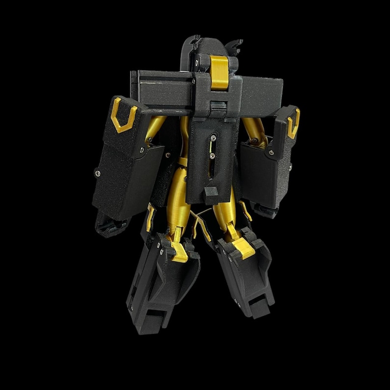 May include: A black and gold robot toy with articulated joints. The robot has a boxy design with black panels and gold-coloured limbs and accents. The toy is standing against a black background.