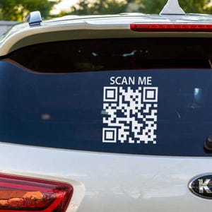 Może przedstawiać: Biała naklejka z kodem QR na tylnej szybie samochodu. Naklejka zawiera tekst "SCAN ME" nad kodem QR. Samochód jest biały z ciemnoniebieską szybą.