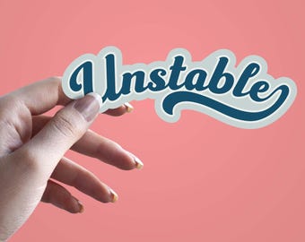Pode incluir: Um adesivo com a palavra "Unstable" em uma fonte retrô, com um esquema de cores verde-azulado e branco. O adesivo é segurado por uma mão contra um fundo rosa.