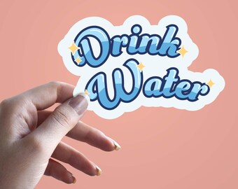 Może przedstawiać: Naklejka z napisem "Drink Water" w stylu retro, niebieską czcionką z białym obrysem. Naklejka ma jasnoniebieski cień i małe żółte akcenty w kształcie gwiazd. Naklejka jest trzymana przez dłoń na brzoskwiniowym tle.