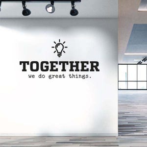 Puede incluir: Una pared blanca con la palabra "TOGETHER" en negrita y letras negras, encima de la frase "we do great things". Un icono de bombilla está encima de la palabra. La habitación tiene un suelo de madera y focos.