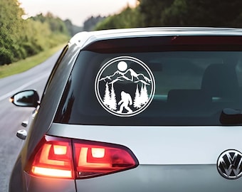 May include: White vinyl decal depicting a Bigfoot silhouette in a mountain and forest scene, with a sun and a circular border. The decal is on the rear window of a silver car, with the word "GOLF" visible.