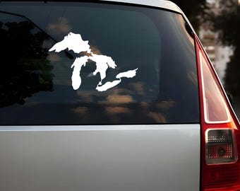 Op de afbeelding: Witte vinylsticker van de Grote Meren op een autoruit. De sticker toont de omtrek van de vijf meren: Superior, Michigan, Huron, Erie en Ontario. De sticker is aangebracht op de achterruit van een zilveren auto.