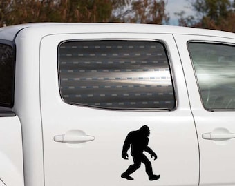 May include: A black Bigfoot silhouette decal is affixed to the side of a white truck. The decal depicts the legendary creature in a walking pose, adding a touch of mystery and outdoor adventure to the vehicle's appearance.