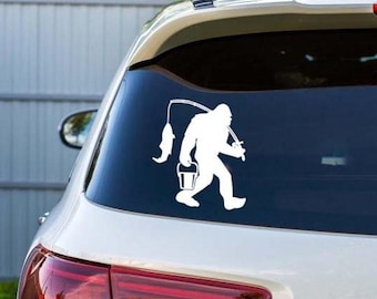 May include: White vinyl decal of Bigfoot, carrying a fishing rod with a fish and a bucket. The sticker is applied to the rear window of a white car. The design is a silhouette.