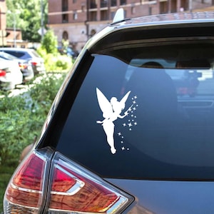 May include: A white vinyl decal of a fairy with outstretched wings and a wand, surrounded by stars. The decal is applied to the rear window of a car, creating a whimsical and decorative accent. The fairy design adds a touch of fantasy.