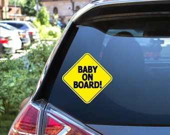 May include: A yellow diamond-shaped sticker with the text "BABY ON BOARD!" in black, affixed to the rear window of a gray car. The sticker is a safety measure to alert other drivers.