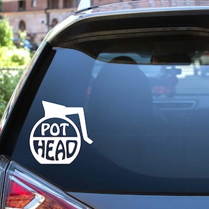 May include: White vinyl decal of a stylized grenade with the words "POT HEAD" in a bold, rounded font. The decal is affixed to the rear window of a vehicle. The design is simple and graphic.