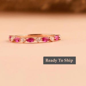 Puede incluir: Un anillo de oro rosa con piedras rosas en forma de marquesa alternadas con pequeñas piedras redondas y transparentes. El anillo está sobre una superficie rosa claro. El texto "Ready To Ship" está en un rectángulo gris oscuro.