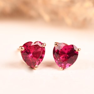 Puede incluir: Un par de pendientes de botón con piedras de color rosa intenso en forma de corazón facetado y montura metálica. Cada piedra está sujeta por pequeñas garras en la parte superior e inferior, mostrando una superficie vibrante y reflectante.
