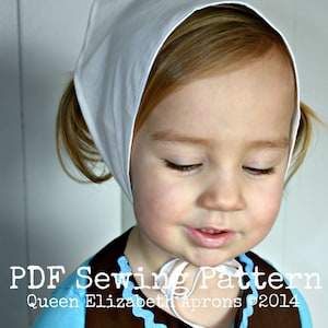 May include: A young child wearing a white bonnet and a blue and brown apron. The apron has a blue wavy trim. The text "PDF Sewing Pattern" and "Queen Elizabeth Aprons ©2014" are visible on the image. The child has blonde hair and is looking down.