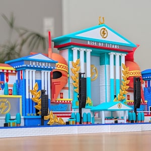 Könnte beinhalten: Ein mehrfarbiges Architekturmodell mit einem zentralen Tempelbau und der Aufschrift "RISE OF TITANS" auf dem Giebel. Das Design umfasst blaue, weiße, gelbe und orangefarbene Elemente, goldene Lorbeerakzente und zwei große orangefarbene Helme.