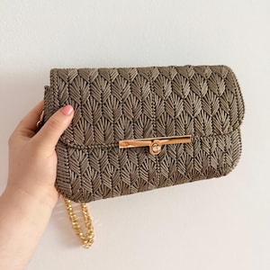 May include: A brown clutch with a gold-colored chain strap and a gold-colored clasp. The clutch has a textured, woven pattern. The bag is rectangular and appears to be made of a soft material.