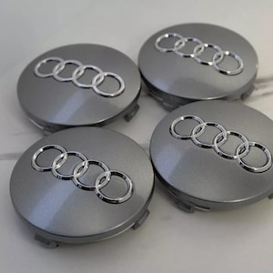 Può includere: Quattro coprimozzi Audi grigi con il logo Audi argentato. I coprimozzi sono rotondi e hanno una finitura metallica. Il logo Audi è un insieme di quattro anelli intrecciati.