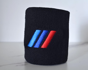 Peut inclure: Poignet noir avec des rayures brodées bleues, bleu foncé et rouges. Le bracelet est fait d'un matériau doux et absorbant, idéal pour le sport ou un usage quotidien. Le design est un logo automobile classique.
