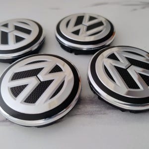 Może przedstawiać: Zestaw trzech ceramicznych kubków z nakrapianym, matowym wykończeniem. Kubki są w odcieniach kremu, jasnoszarym i ciemnoszarym. Każdy kubek ma prosty, minimalistyczny design.