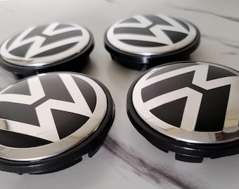 Peut inclure: Quatre enjoliveurs noirs et argentés avec le logo Volkswagen. Les enjoliveurs ont un centre noir, un bord argenté et un emblème VW blanc. Les enjoliveurs sont ronds et ont une base en plastique noir.