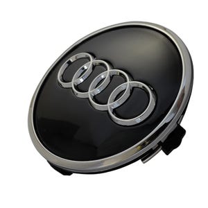 Könnte beinhalten: Ein schwarzes und silbernes Autoemblem mit dem Audi-Logo. Das Emblem ist oval geformt mit einer glänzenden schwarzen Oberfläche und einer silbernen Umrandung. Das Audi-Logo besteht aus vier ineinandergreifenden silbernen Ringen.
