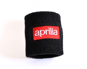 Peut inclure: Un bracelet de poignet noir avec le mot "aprilia" en blanc sur un patch rectangulaire rouge. Le bracelet est fait d'une matière épaisse et absorbante.